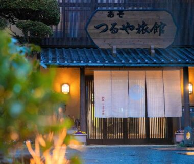Noren curtain and wooden sliding doors at AsoTsuruya ryokan entrance, warm lanterns and stone pathway in Kumamoto