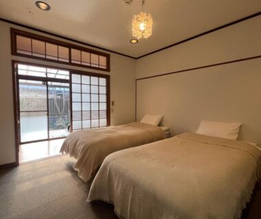 Twin beds and shoji sliding doors in a minimalist Japanese guestroom at Assi House Oita