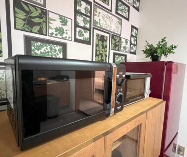 Microwaves and red mini fridge on wooden cabinet with botanical wall prints at Assi House, Ōita
