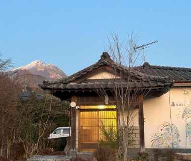 Wooden entrance and tiled roof at Assi House ryokan in Ōita, Kyūshū with mountain backdrop