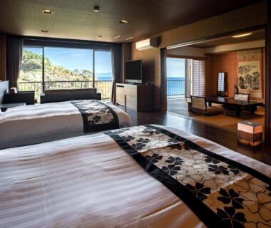 Warm wooden interior twin room with low seating and large windows overlooking coastal bay at Atagawa Prince Hotel Shizuoka