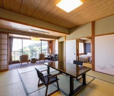 Tatami room with low table, chairs, shoji screens and balcony overlooking greenery at Atagawa Prince Hotel, Shizuoka