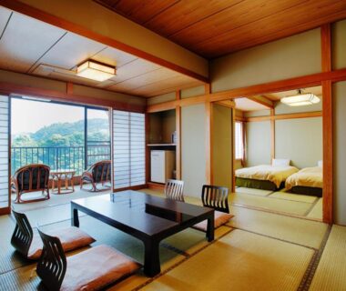 Traditional tatami room with low table, futon area and balcony overlooking green hills at Atagawa Prince Hotel, Shizuoka
