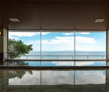 Indoor onsen bath with floor-to-ceiling windows overlooking calm ocean horizon at Atagawakan in Shizuoka