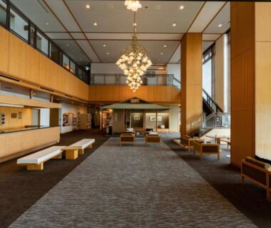 Spacious lobby at Atagawakan with chandelier, wooden columns, reception counter and seating, Shizuoka