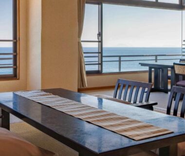 Tatami dining area with low table and chairs facing ocean-view windows at Atagawakan, Chūbu Shizuoka