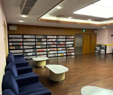Spacious lounge with bookshelves, blue armchairs and low tables at Atami New Fujiya Hotel in Shizuoka