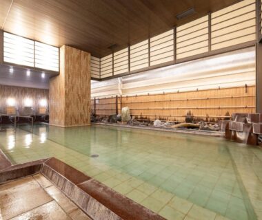 Spacious indoor onsen with tiled pool and wooden accents at Atami New Fujiya Hotel, Shizuoka, Japan