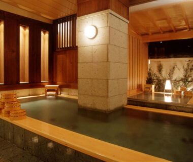 Indoor onsen with wooden surrounds, stone pillar, stacked buckets and small garden view at Atami Onsen Sakuraya Ryokan