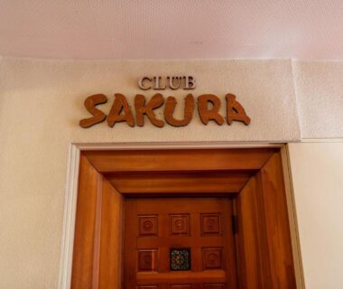 Carved Club Sakura sign above a wooden entrance door at Atami Sakuraya Ryokan, Shizuoka
