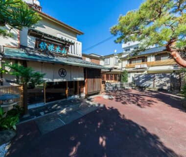 Ryokan courtyard with wooden facade, latticed windows, entrance path and pine tree at Atami Onsen Yamaki Ryokan, Shizuoka