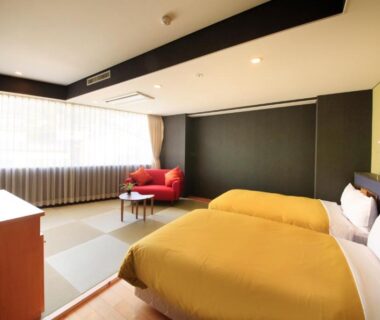 Twin beds with yellow covers, tatami seating area, low table and red armchair in Atami Tensui room, Shizuoka