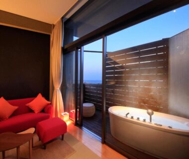 Room with balcony soaking tub, red lounge chair and glass sliding doors at Atami Tensui Shizuoka