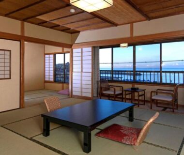 Traditional tatami room with low table, cushions, shoji screens and balcony overlooking coastal water in Atami, Shizuoka