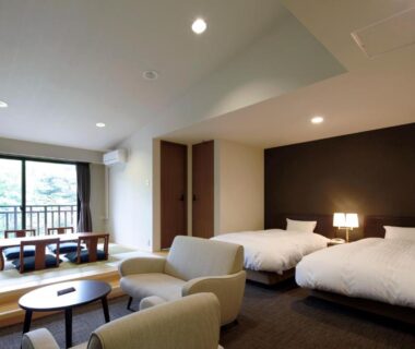 Spacious room with tatami seating, twin beds, lounge chairs and balcony overlooking trees at Auberge Cosmos, Ōita