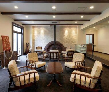 Carved wooden armchairs arranged around low table in ryokan lounge with stone fireplace backdrop at Auberge Cosmos Ōita