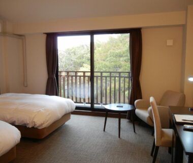 Bright twin room with balcony overlooking trees at Auberge Cosmos, Ōita Kyūshū