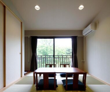 Tatami room with low table and floor cushions, sliding doors and balcony overlooking trees at Auberge Cosmos in Ōita