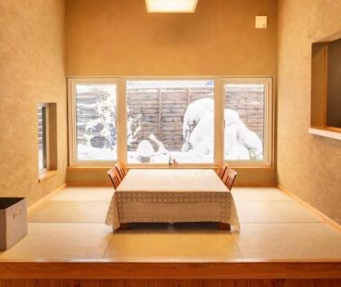 Raised tatami seating area with low table, wooden ceiling and snowy courtyard view at Auberge Ninguruforet Hokkaidō