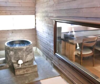 Stone soaking tub in wooden room with tatami mat and window into dining area at Auberge Ninguruforet, Hokkaidō