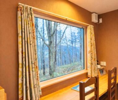 Wooden desk and chairs by large window at Auberge Ninguruforet, birch trees outside in Hokkaidō