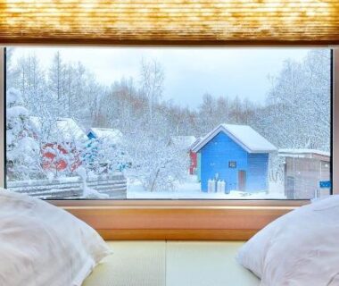 Tatami floor with futon beds facing snowy window with blue house and tree-lined landscape