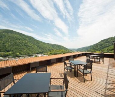 Wooden rooftop terrace with tables and chairs overlooking verdant hills at Aura Tachibana in Kanagawa, Kantō