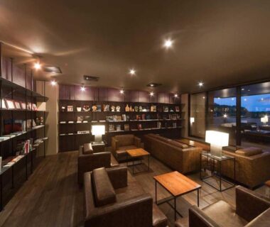 Evening lounge with leather sofas, bookshelves, low tables and lamps at Aura Tachibana in Kanagawa