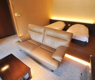 Twin beds with leather sofa and low table at Aura Tachibana in Kanagawa