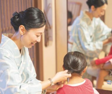 Woman in kimono styling a young girl's hair by mirror inside Awakan ryokan in Hyōgo Kansai