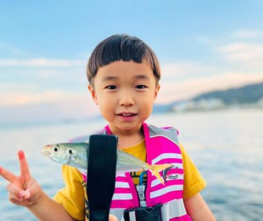 Child in life jacket holding fish on boat near shore Awakan Hyōgo