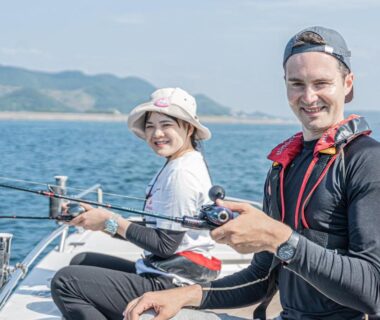 Two people fishing from a small boat with coastal hills in background near Awakan, Hyōgo, Kansai