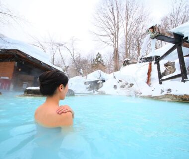 Guest soaking in milky-blue outdoor onsen surrounded by snow at Awanoyu in Nagano
