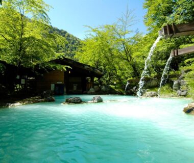 Turquoise outdoor onsen pool with wooden waterfall at Awanoyu in Nagano