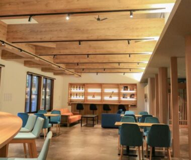 Warm wooden lounge with exposed beams counter seating and teal chairs at Awazuonsen Kitahachi in Ishikawa Chubu