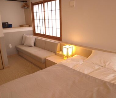 Tatami flooring with low sofa, twin beds, shoji screen window and bedside lamp in a ryokan room