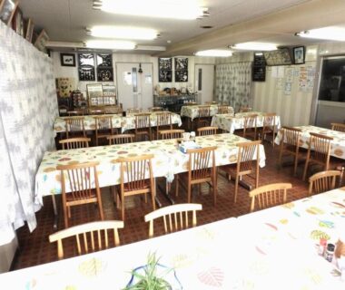 Long communal dining room with tablecloths, wooden chairs and serving counter at Azuma no Yu in Nagano