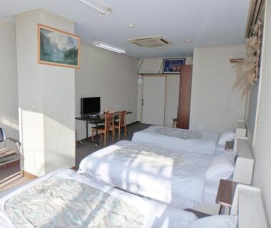 Spacious sunlit guest room with multiple beds, TV, desk, and window at Azuma no Yu, Nagano