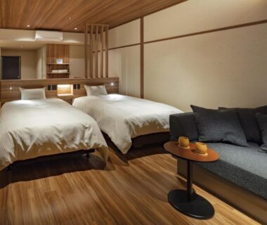 Warm wooden interior with twin beds, shoji screens, low tea table and sofa in Azumakan ryokan, Fukushima