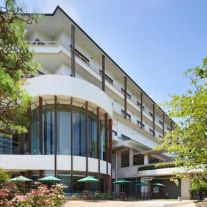 White multi-story ryokan with curved glass facade, balconies, outdoor umbrellas and surrounding trees in Fukushima