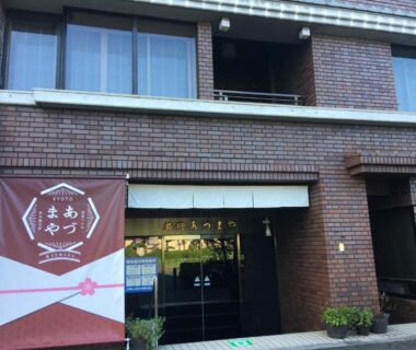 Brick facade and glass entrance of Azumaya Ryokan with banner and potted plants, Kyoto