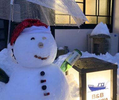 Snowman under umbrella beside illuminated B&B MIKAWA lantern at snowy entrance area, Kanazawa, Ishikawa