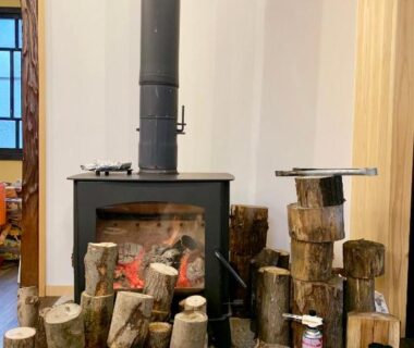Freestanding wood stove surrounded by stacked firewood logs in ryokan interior at B&B MIKAWA, Kanazawa, Ishikawa