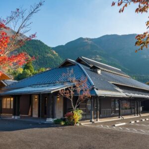Traditional tiled-roof ryokan Baien entrance with autumn maples and mountain backdrop in Ōita, Kyūshū