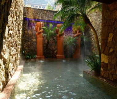 Steam rising over a stone bath with carved wooden statues at Balinese onsen ryokan Hakone Airu, Kanagawa