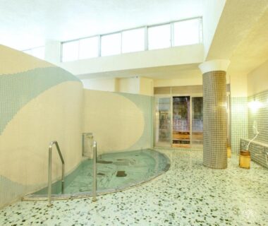 Mosaic-tiled indoor onsen with circular bath, handrails and wooden stools at Bansuirou Fukuzumi in Kanagawa