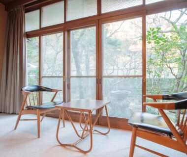 Tatami room with two wooden chairs and low table by sliding windows overlooking trees