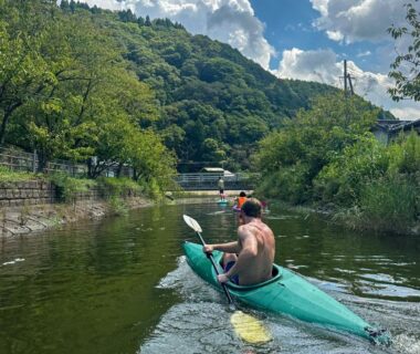 Kayakers paddling a calm river near Base House Kinosaki in Hyōgo, Kansai with green hills