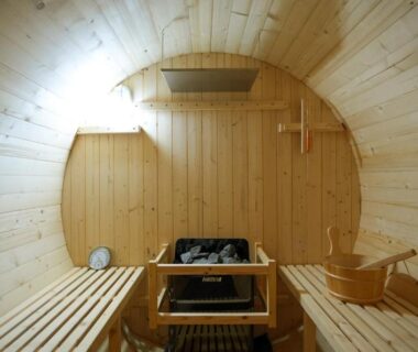 Wooden barrel sauna interior with benches, central heater and water ladle at Base House Kinosaki, Hyōgo