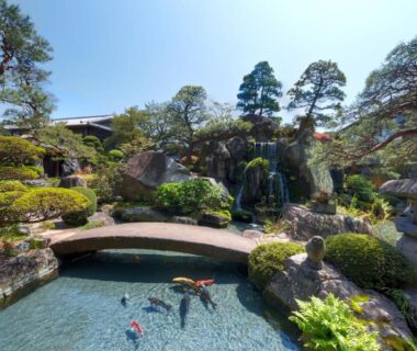 Koi pond with curved stone bridge, lanterns and trimmed pine trees at Kagetsu in Yamanashi